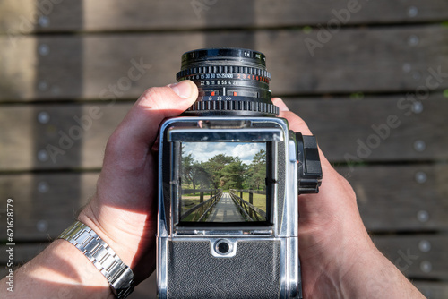 A man takes a photo of a path through nature with a vintage viewfinder camera.