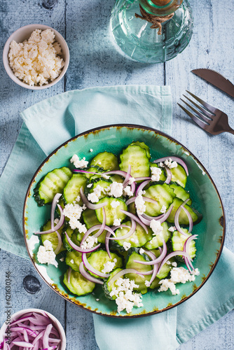 Diet salad of cucumbers, red onions and ricotta on a plate on the table top and vertical view