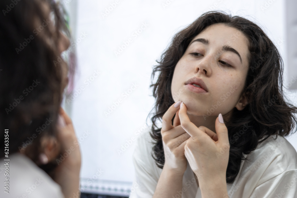 Unhappy young latin lady in white bathrobe standing in front of mirror in bathroom, removing blackheads from her face skin. Acne, pimples, problem skin care concept Unhappy young latin lady in white bathrobe standing in front of mirror in bathroom, removing blackheads from her face skin. Acne, pimples, problem skin care concept