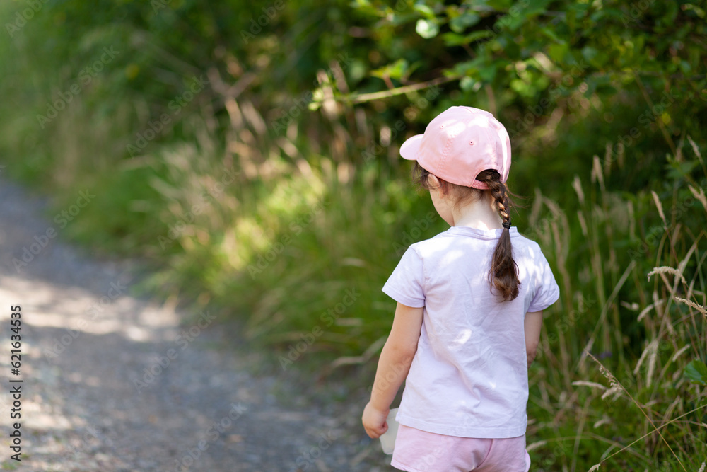 Adorable little girl wearing baseball cap outdoors on warm and sunny summer day