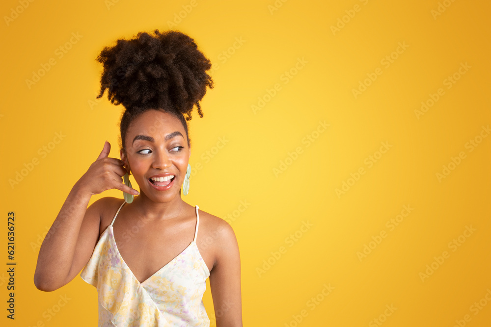 Fototapeta premium Cheerful millennial african american lady in dress making call me gesture, flirting, isolated on yellow background