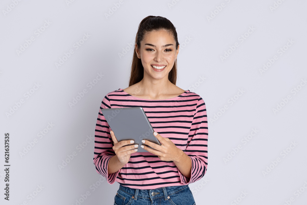 Happy brunette millennil woman using digital tablet on grey Happy brunette millennil woman using digital tablet on grey