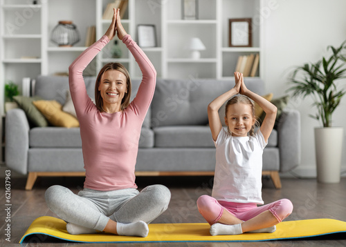 Happy young mother and little daughter in sportswear practicing yoga at home