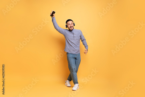 Cheerful asian man in wireless headphones listening music on smartphone and dancing