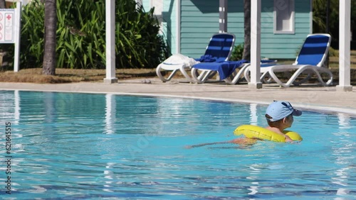On a sunny day,a child swims in the hotel's children's pool.The concept of holidays with children.A boy in a swimming circle splashes his feet in the water.Summer holidays at the resort