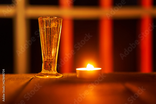 Still life picture of vintage shot glass and small burning tea candle on the wooden table on terrace. Picture is taken in the summer midninght. Silent scene for meditation and thinking about ourselves photo