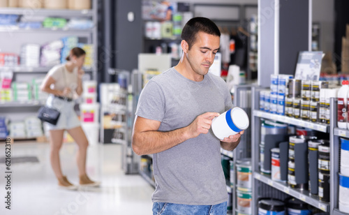 Male customer chooses can of paint in a hardware store