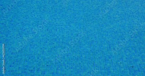 Blue tiled swimming pool with water wave ripples reflecting sunlight, background texture.