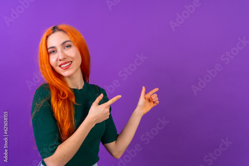 Red-haired woman in studio photography making the gesture of pointing on a purple background