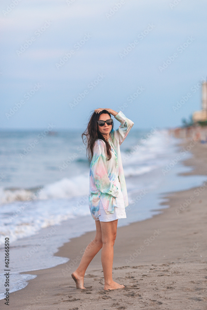 Young happy woman on the beach enjoy her summer vacation. Woman walking along the sea in evening. 