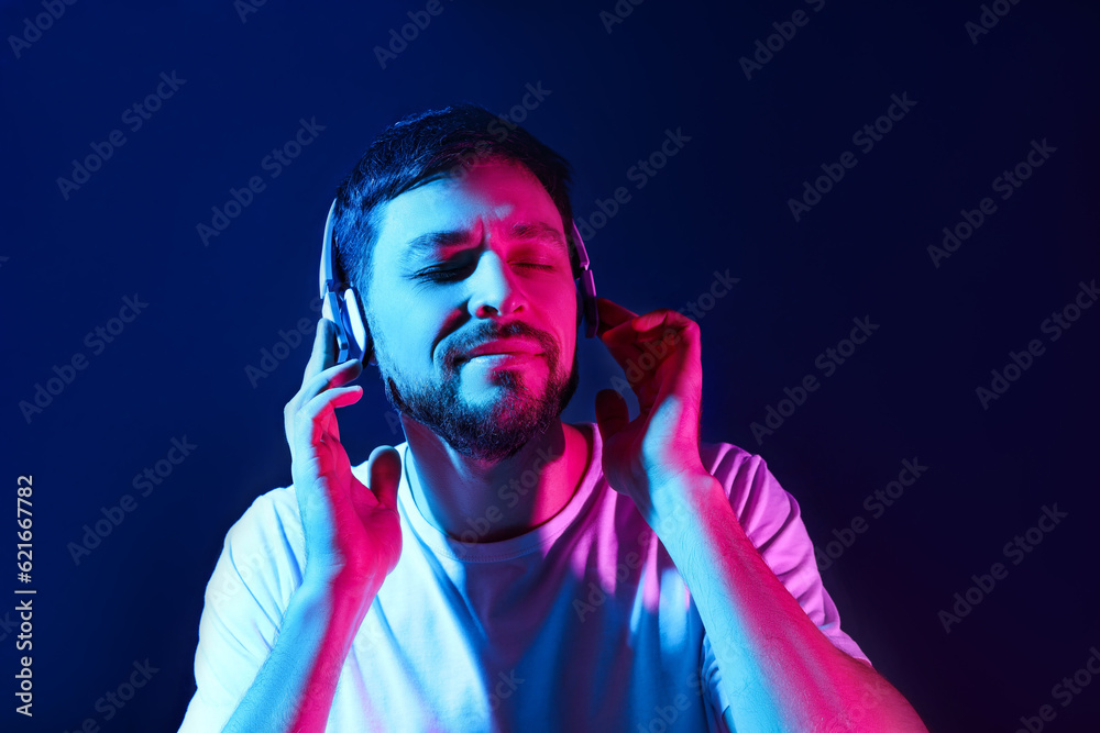 Handsome man in headphones enjoying music in neon lights against dark blue background Handsome man in headphones enjoying music in neon lights against dark blue background
