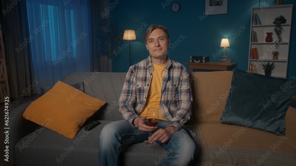 Portrait of a man with a glass of wine sitting on the sofa in front of the TV close up. A man is watching a dramatic movie or a touching home video. Portrait of a man with a glass of wine sitting on the sofa in front of the TV close up. A man is watching a dramatic movie or a touching home video.