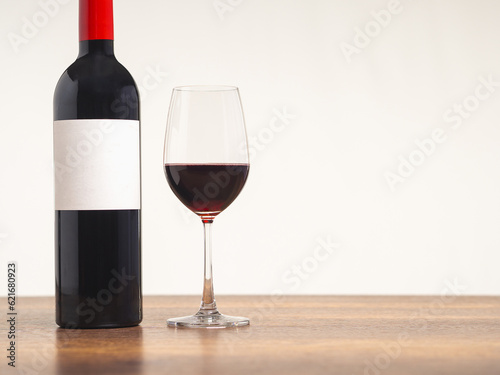 A Wine bottle and a glass of red wine are on the table against a gray background.
