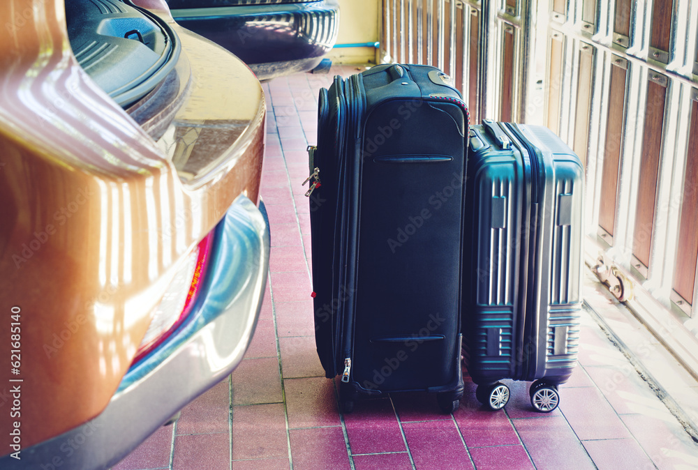 Two luggage stand on the floor close to the rear car in a parking lot