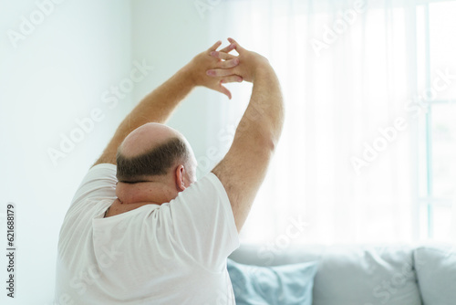 Caucasian white man wake up from the bed in morning and sitting beside the bed then doing a stretch oneself. A cozy lazy overweight fat man sitting on the bed after woke up in morning.