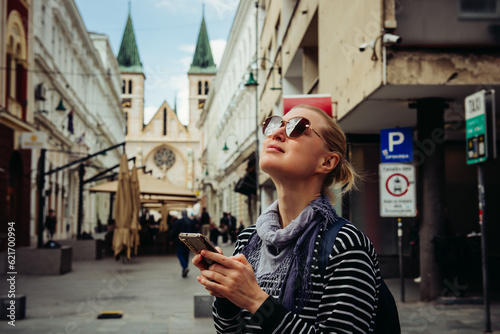 A young female traveler walks through the streets of a European city using a smartphone. Blonde in dark glasses and with a backpack, independent walks to the sights