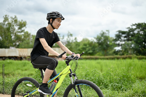 A happy man in sportswear and a bike helmet rides a bike along country roads.