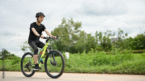 A determined Asian man in sportswear and a bike helmet rides a bike along country roads.