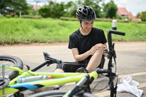 An injured young Asian male cyclist in sportswear and a bike helmet fell off the bike