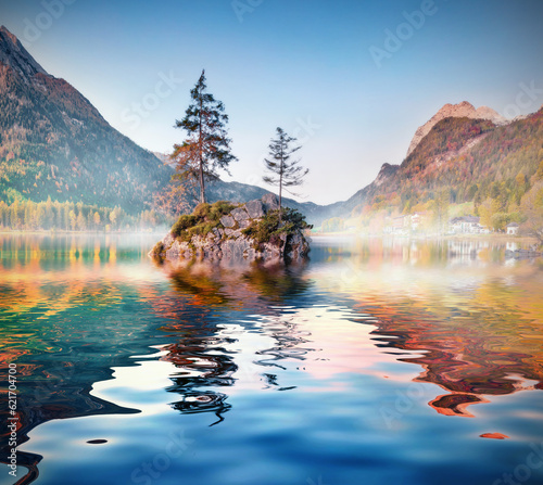 Small islets with fir tree reflected in the calm waters of Hintersee lake, Germany. Misty autumn view of Bavarian Alps with Hochkalter peak on background. Beauty of nature concept background.