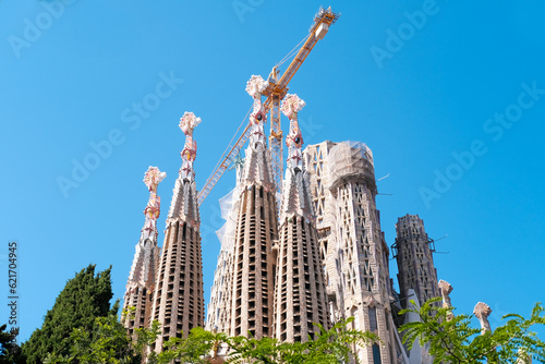 Barcelona, Spain - May 27, 2022. The famous and beautiful cathedral Sagrada Familia by architect Antonio Gaudi, Catalonia. Bottom view from a green park against a clear blue sky. Copy space.