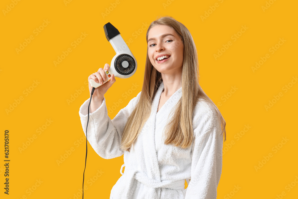 Young blonde woman with hair dryer on yellow background Young blonde woman with hair dryer on yellow background