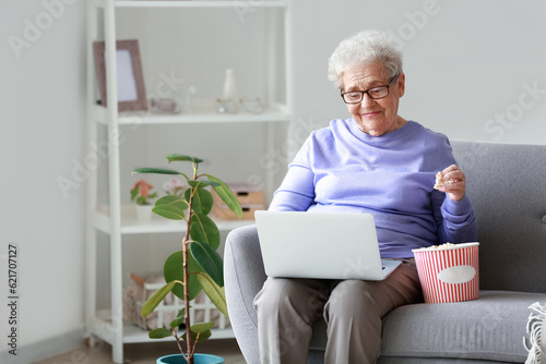 Senior woman with laptop and popcorn watching video at home