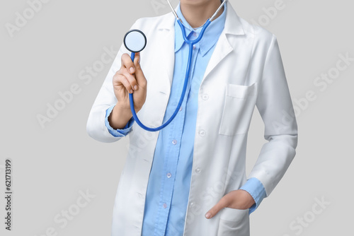 Female doctor in white coat with stethoscope on grey background