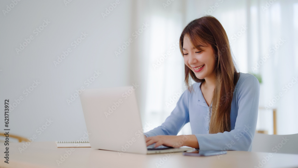 Young asian woman working at home. Happy female using computer laptop on desk at house Young asian woman working at home. Happy female using computer laptop on desk at house