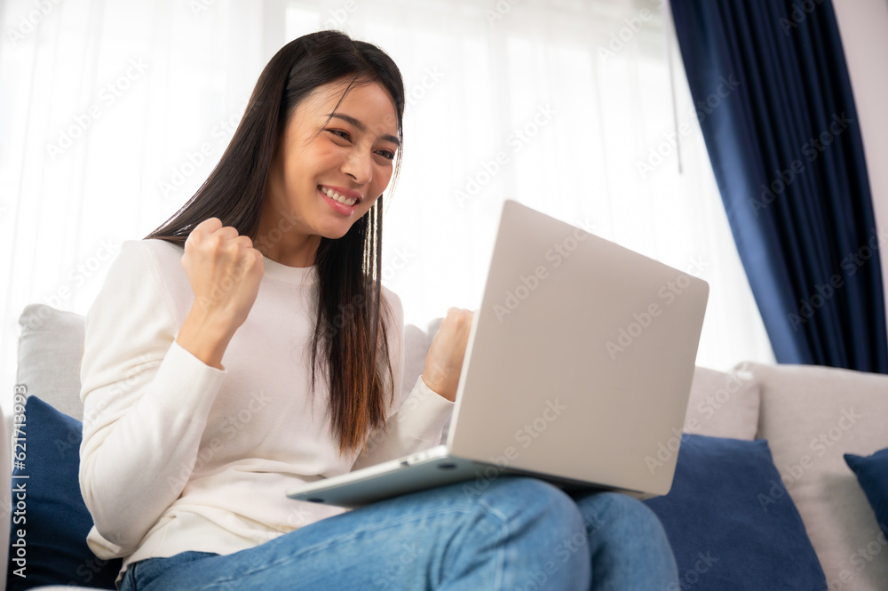 Funny euphoric young asian woman celebrating winning or getting ecommerce shopping offer on computer laptop. Excited happy girl winner looking at notebook celebrating success Funny euphoric young asian woman celebrating winning or getting ecommerce shopping offer on computer laptop. Excited happy girl winner looking at notebook celebrating success