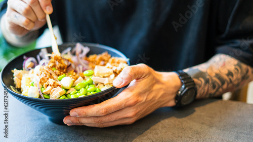 tattooed man holding a poke bowl with edamames and chicken