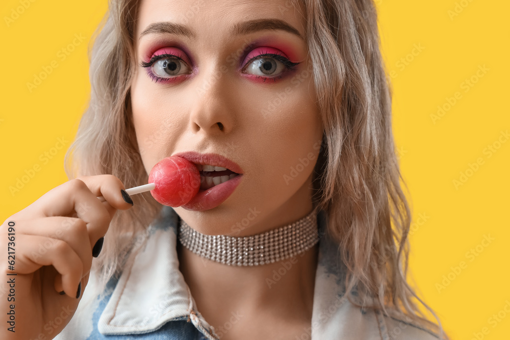 Young woman eating lollipop on yellow background, closeup Young woman eating lollipop on yellow background, closeup