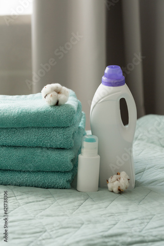 White plastic packaging with laundry detergent, liquid washing powder, conditioner, bleach, stain remover for clothes, terry towels and cotton flowers.