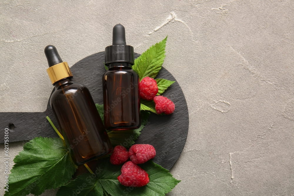 Board with bottles of cosmetic raspberry oil on grey table Board with bottles of cosmetic raspberry oil on grey table