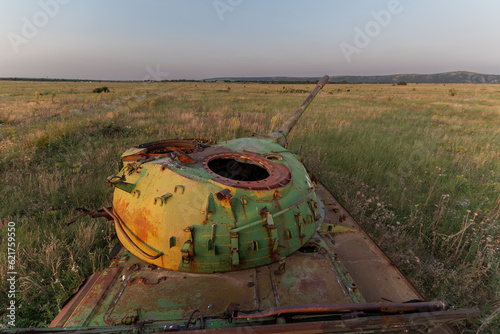 Destroyed rusted, abandoned and buned out battle tank in the green fields at sunset time. You can use this image for example war articles like ukraine vs Russia war. photo