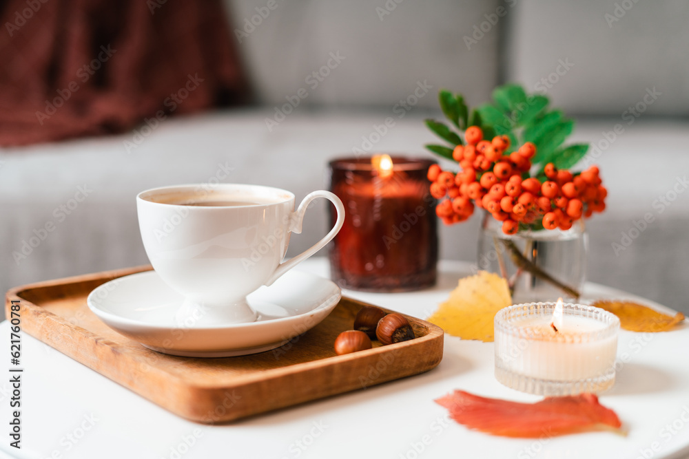 Still life book, candle, rowan berry and a cup of tea or coffee in the living room on a table, home decor in a cozy house. Autumn weekend concept, blanket and plaid. Fallen leaves and home decoration