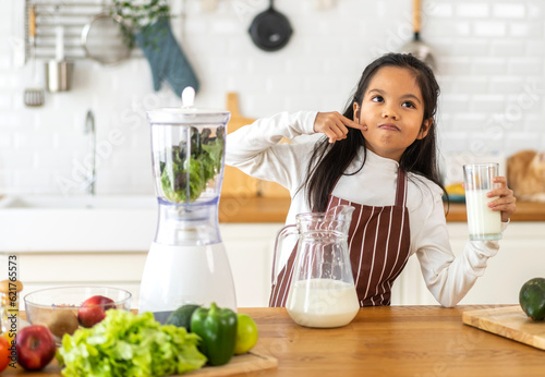 Portrait of enjoy happy little asian child girl smiling having protein breakfast drinking and hold glasses of fresh milk,healthy nutrition,calcium and vitamin,dairy product,strong, growth in kitchen
