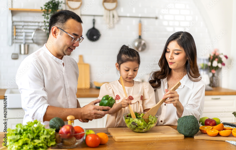 Portrait of enjoy happy love asian family father and mother with little asian girl daughter child having fun help cooking food healthy eat together with fresh vegetable salad ingredient in kitchen