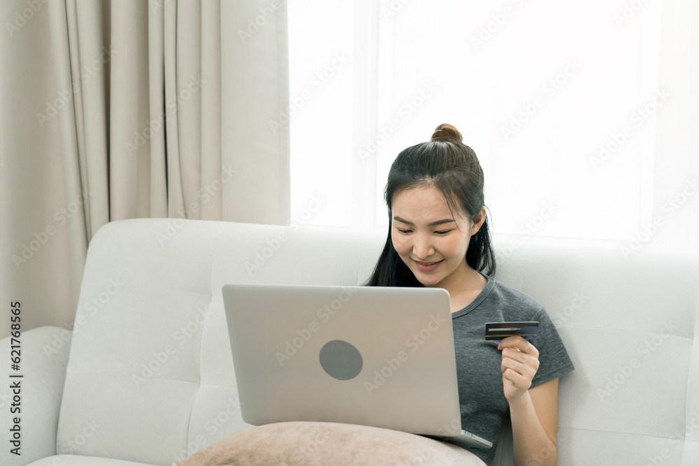Asian woman holding a credit card for online shopping while sitting on the couch while on vacation at home. Asian woman holding a credit card for online shopping while sitting on the couch while on vacation at home.