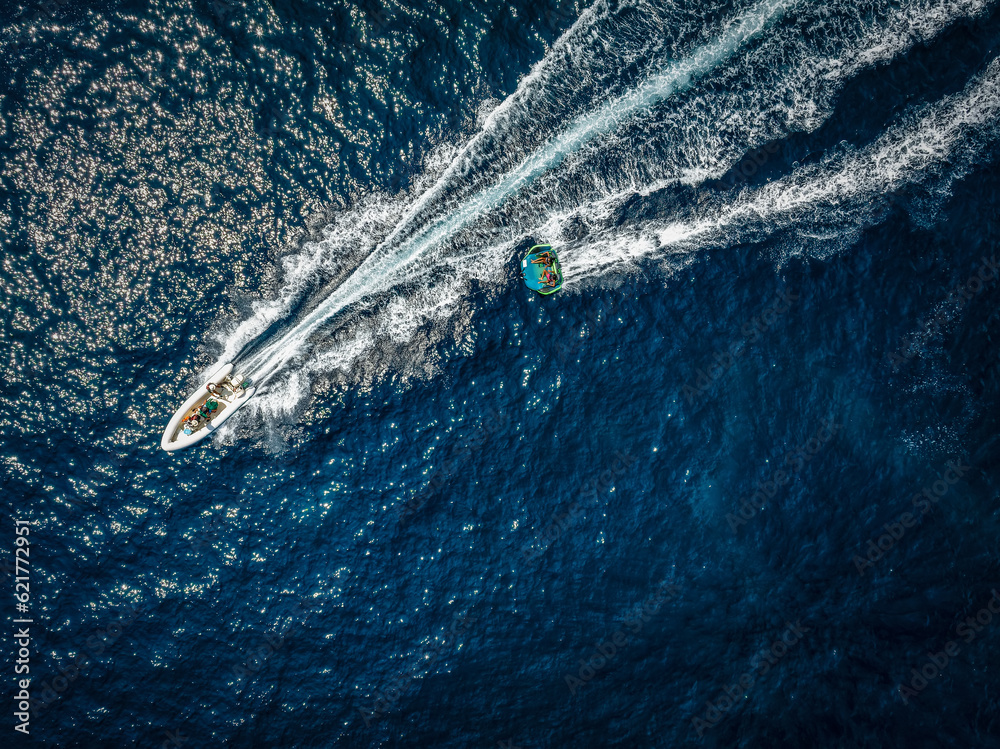 Obraz premium Aerial view of a motor speeboat towing a watersports fun inflatable tube over blue sea