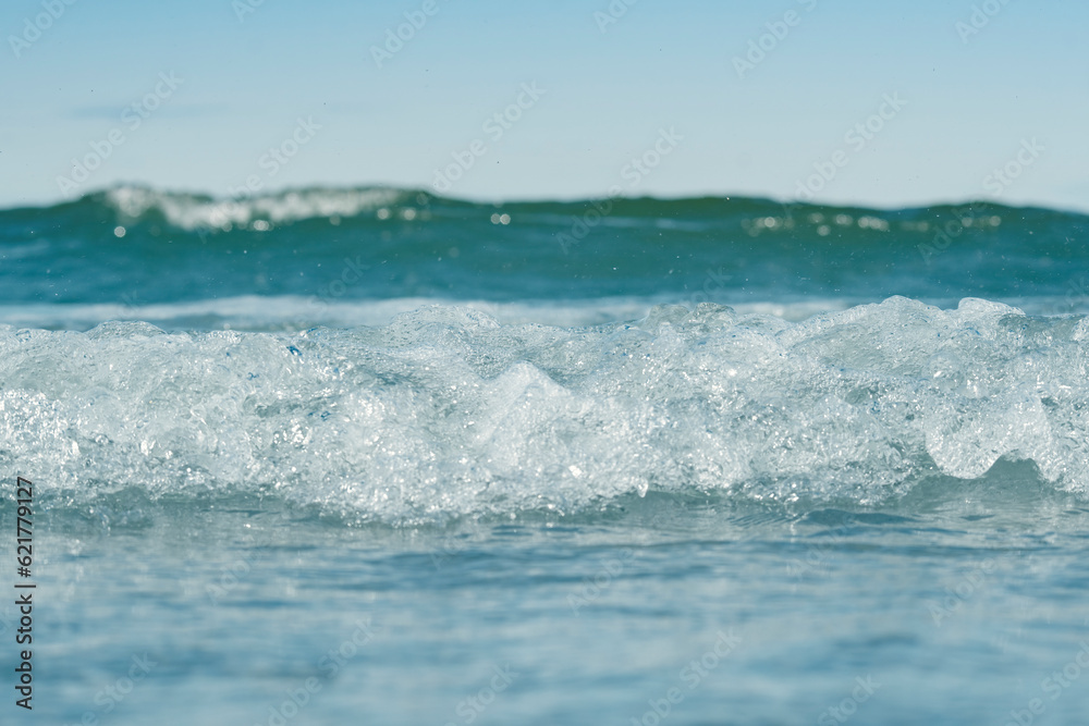 View of seawater with focus on the crest of a wave. Blurred background with low depth of field. Template on the theme of a seaside vacation with blank space for text.