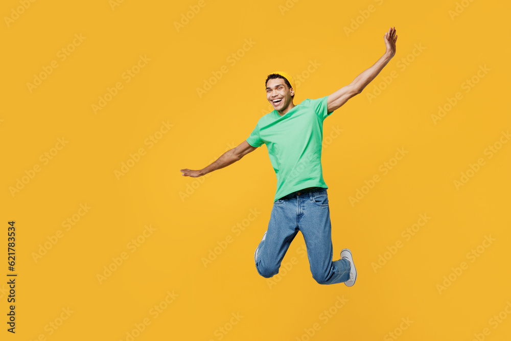 Obraz premium Full body young man of African American ethnicity he wears casual clothes green t-shirt hat jump high with outstretched hands pov flying isolated on plain yellow background studio. Lifestyle concept.