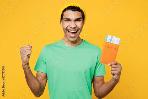Traveler man wearing casual clothes hold passport ticket do winner gesture isolated on plain yellow background. Tourist travel abroad in free spare time rest getaway. Air flight trip journey concept.