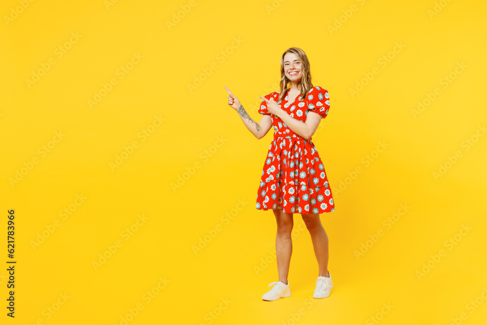 Full body young smiling caucasian woman she wears red dress casual clothes point index finger aside on area mock up copy space isolated on plain yellow background studio portrait. Lifestyle concept. Full body young smiling caucasian woman she wears red dress casual clothes point index finger aside on area mock up copy space isolated on plain yellow background studio portrait. Lifestyle concept.