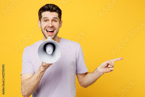 Young man wears light purple t-shirt casual clothes hold in hand megaphone scream announces discounts sale Hurry up point aside isolated on plain yellow background studio portrait. Lifestyle concept.