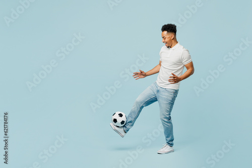 Fototapeta Naklejka Na Ścianę i Meble -  Full body side profile view fun cheerful young man fan wearing t-shirt cheer up support football sport team hit soccer ball on leg watch tv live stream isolated on plain pastel blue color background