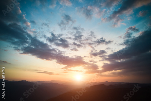 Fototapeta Naklejka Na Ścianę i Meble -  Panoramic view of bright evening sun and dramatic cloudy sky over mountains. Magnificent scenery of mountain hills under colorful evening sky with clouds and setting sun. Beauty of nature concept.