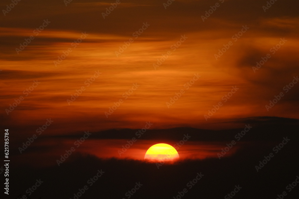 A Radiant Farewell: Half Sun Setting in the Horizontal Orange Sky, Embracing the Coming Darkness