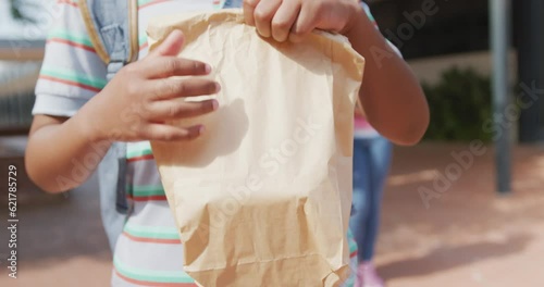 Video midsection of african american schoolboy holding packed lunch outside school photo