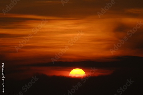 A Radiant Farewell: Half Sun Setting in the Horizontal Orange Sky, Embracing the Coming Darkness